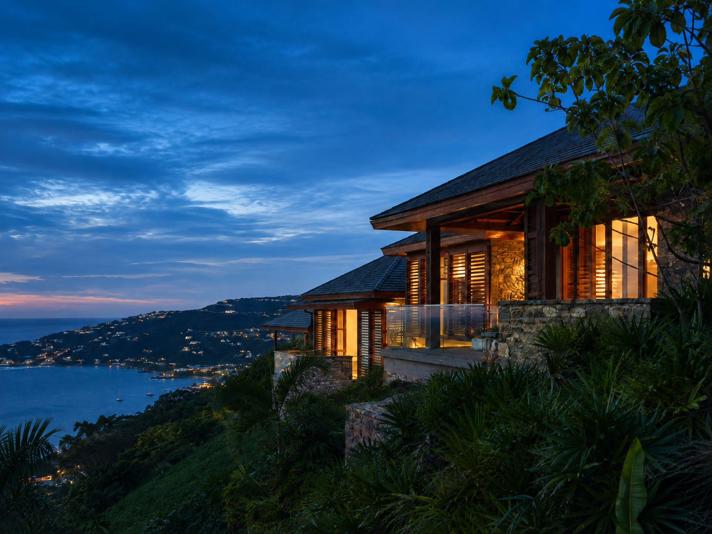 Caribbean hillside home at dusk with lights on